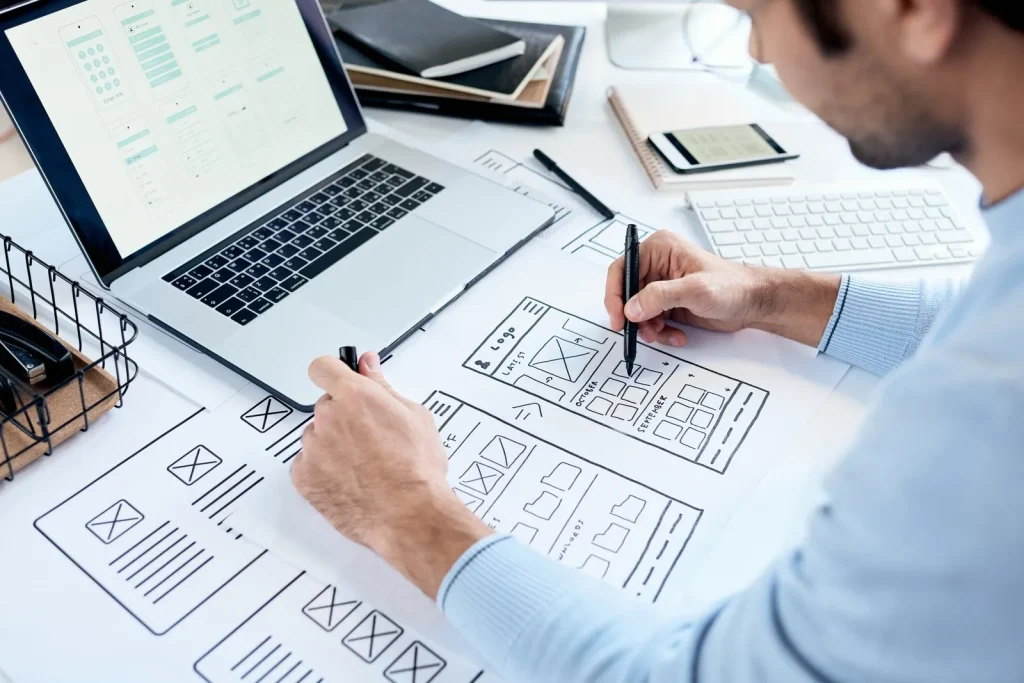 Webdesigner skizziert den Aufbau einer Website neben dem Laptop