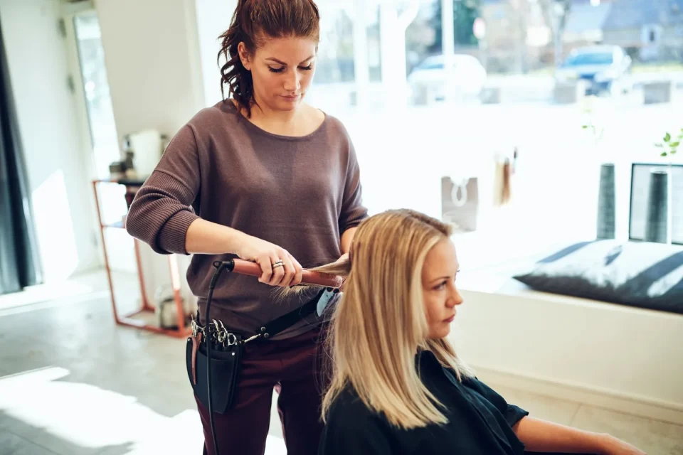 Friseurin stylt die Haare einer Kundin im Salon